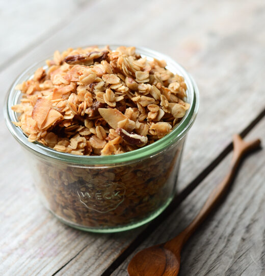 A jar filled with granola with a wooden spoon next to it.