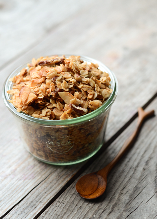 A jar filled with granola with a wooden spoon next to it.