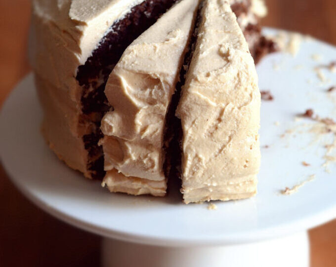 A chocolate layer cake with peanut butter frosting on a cake stand with a few pieces taken out.