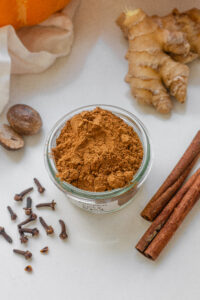 A top down picture of homemade pumpkin spice blend in a small jar with whole spices and a pumpkin around it.