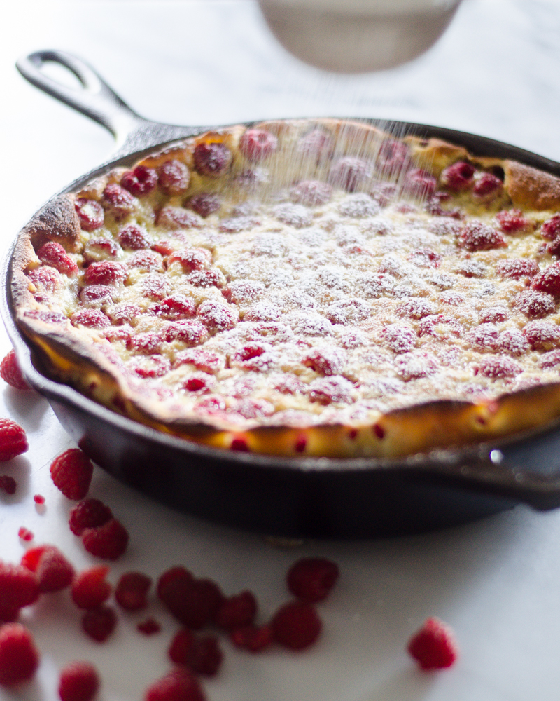 Dusting a Raspberry Clafoutis with powdered sugar.