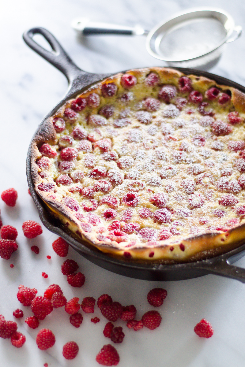 A Raspberry Clafoutis cooked in a cast iron skillet with a dusting of powdered sugar on top.