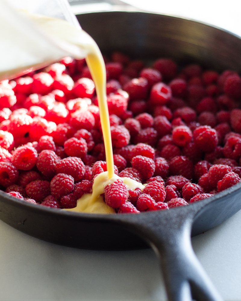 Pouring the batter over the berries in the bottom of the cast iron skillet. 