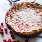 A raspberry clafoutis in a cast iron skillet with powdered sugar dusted on top.