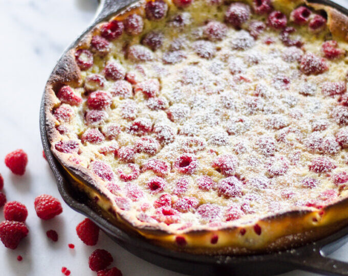 A raspberry clafoutis in a cast iron skillet with powdered sugar dusted on top.