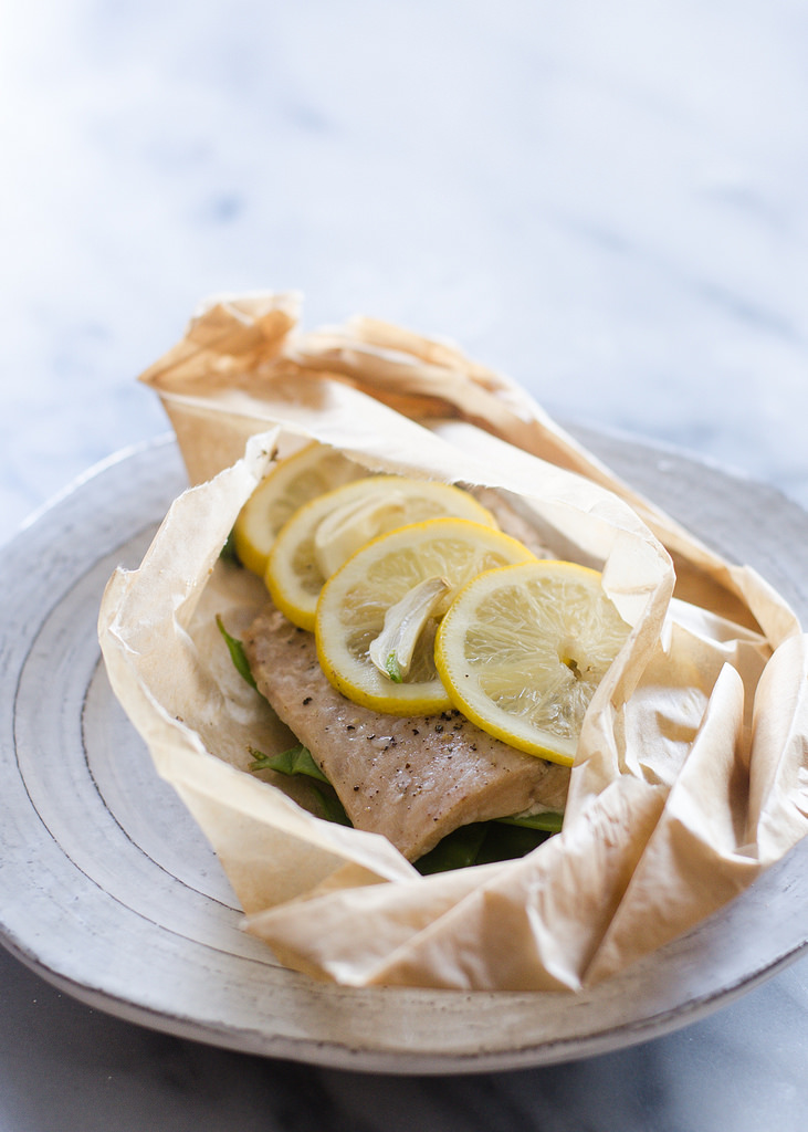 A salmon filet in a piece of parchment paper with snow peas underneath and slices of lemon on top.