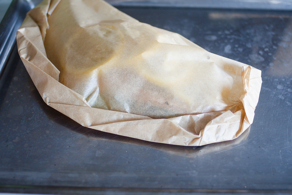 The salmon fillet on a baking sheet all wrapped up in a piece of parchment paper.