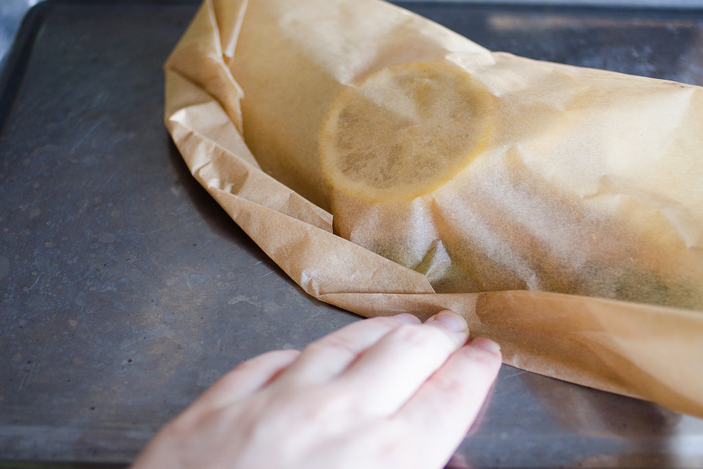 Making small folds along the edge of the piece of parchment paper to seal the salmon en papillote. 