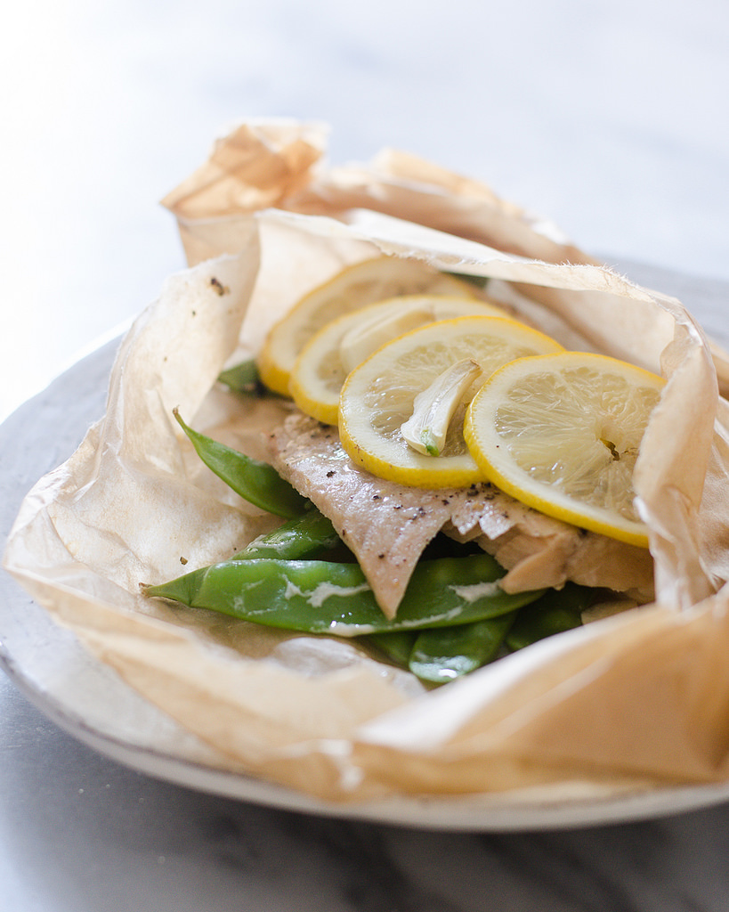 Salmon en Papillote: A salmon filet in a piece of parchment paper with snow peas underneath and slices of lemon on top.