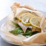 Salmon in a parchment paper packet with snow peas underneath and lemon slices on top.