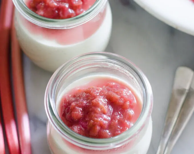 Small jars filled with Russian Cream with a rhubarb compote on top with rhubarb stalks off to the side.