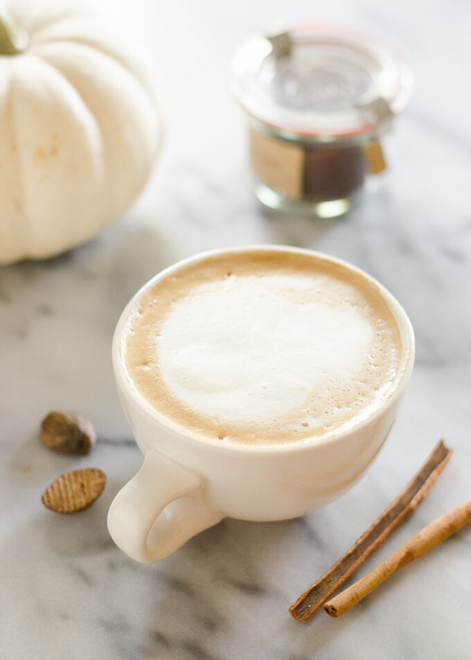 A mug of PSL with cinnamon sticks and pumpkin around it.