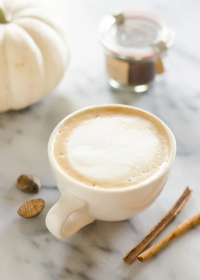 A mug of PSL with cinnamon sticks and pumpkin around it.