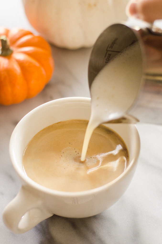 Pouring the frothed milk on top of the coffee mixture to make a Homemade Pumpkin Spice Latte