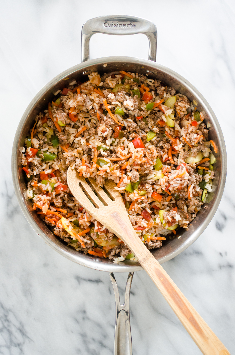 All of the ingredients for the filling part of the easy stuffed pepper casserole in a large skillet with a wooden spoon. 