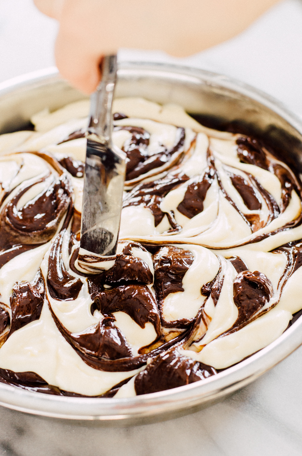 Swirling the cheesecake batter and chocolate batter together with a butter knife before baking the chocolate marbled cheesecake. 