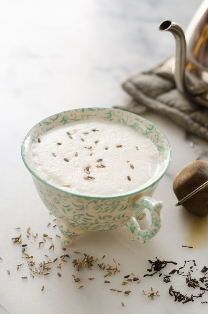 A London Fog Tea Latte (AKA Earl Grey Latte) in a pretty teacup with a tea kettle behind it. 