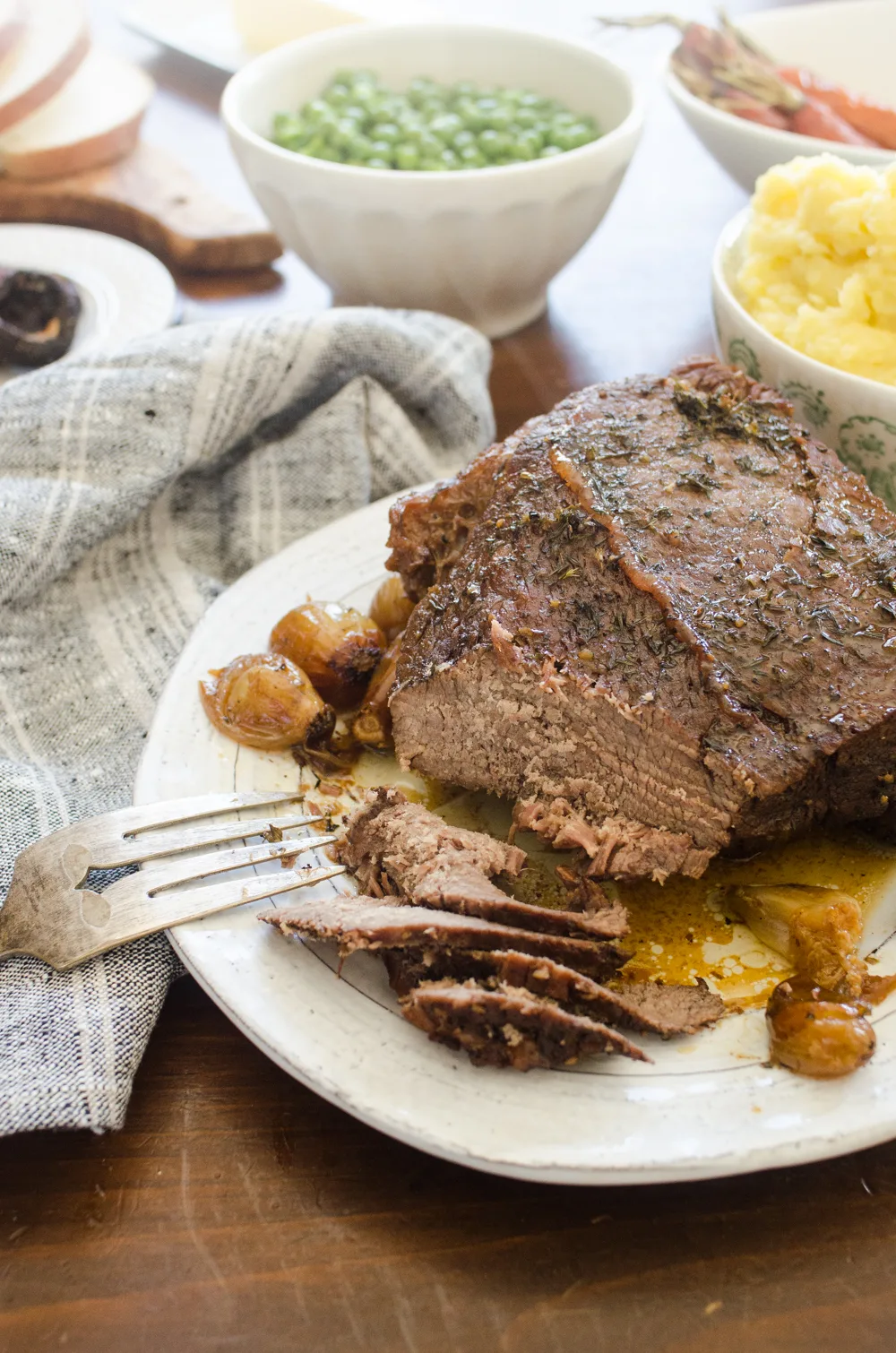 A plate of grass fed chuck roast with side dishes around it.