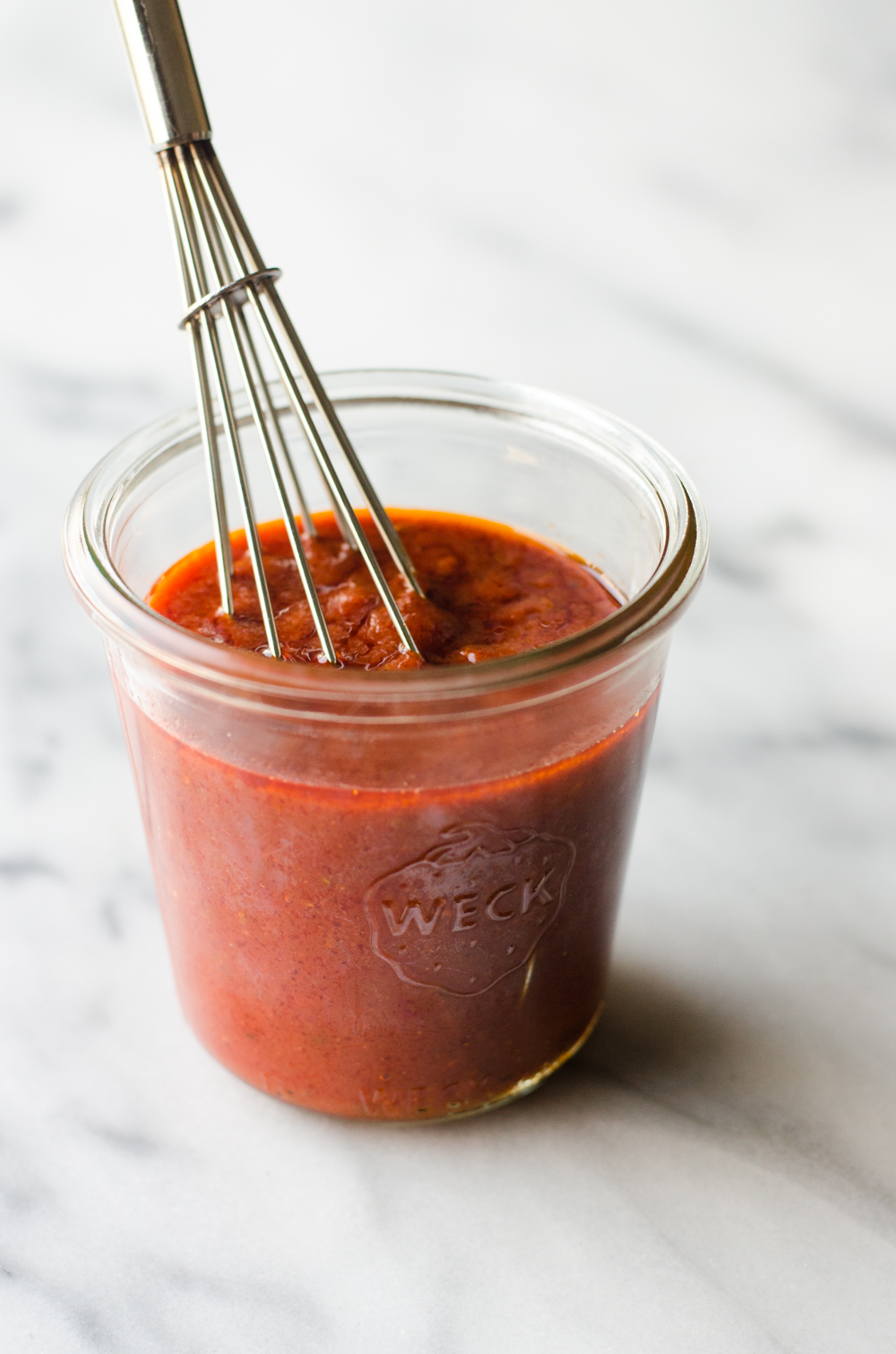 A jar of pizza sauce with a whisk in it.