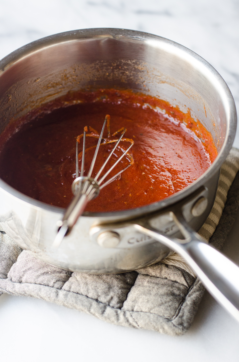 Homemade pizza sauce in a small saucepan with a whisk in it. 