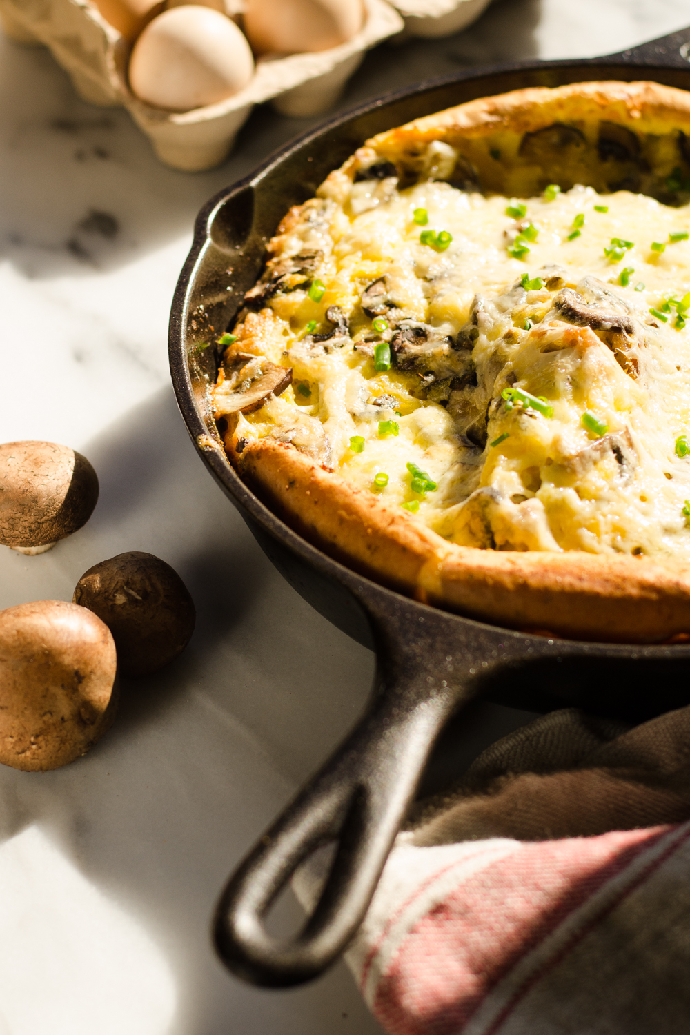 A pan of savory Dutch baby with eggs in the background and a tea towel in the foreground.