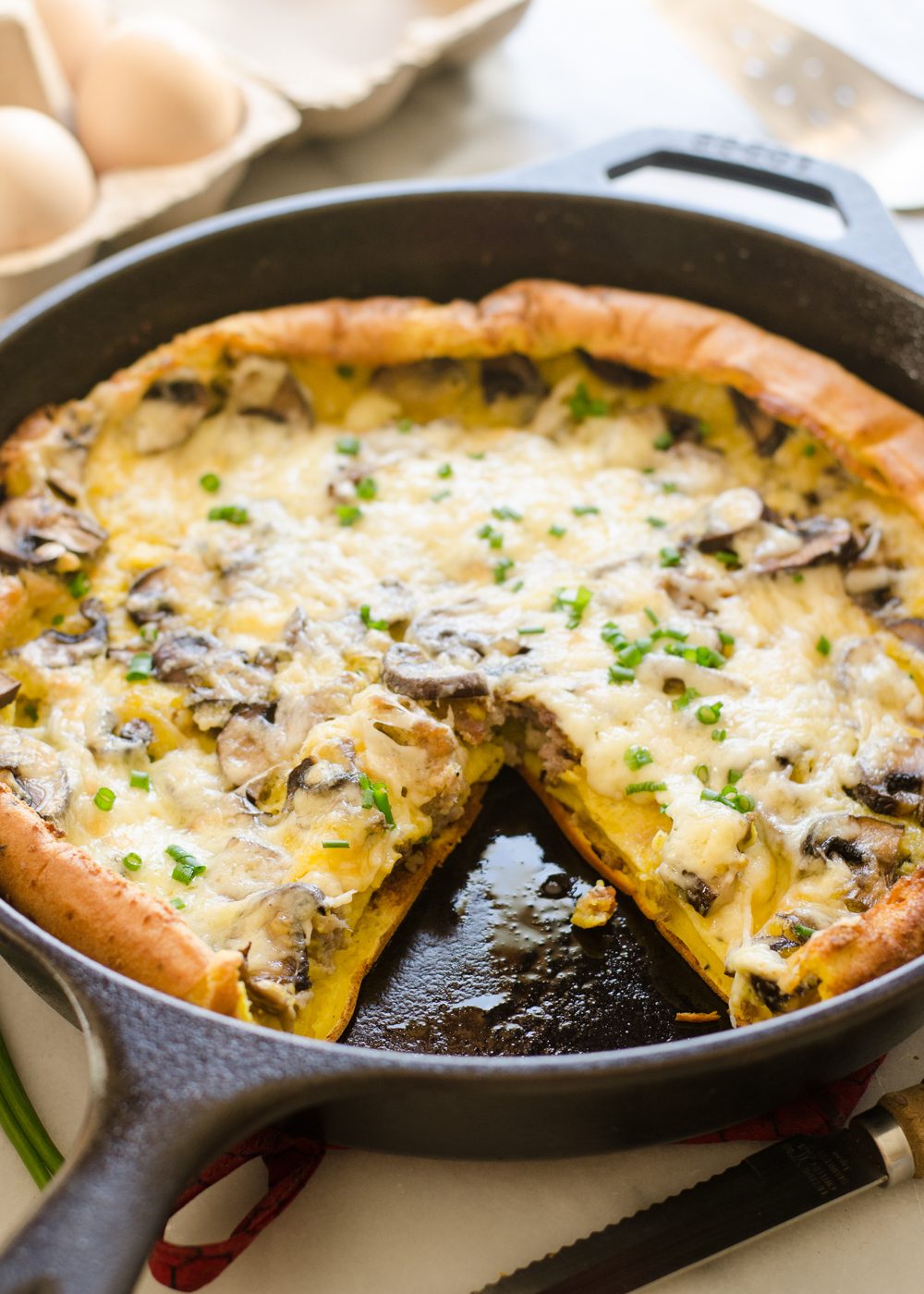 A pan of savory Dutch baby with eggs in the background and a tea towel in the foreground.