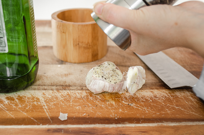 Grating pepper on top of the head of garlic.