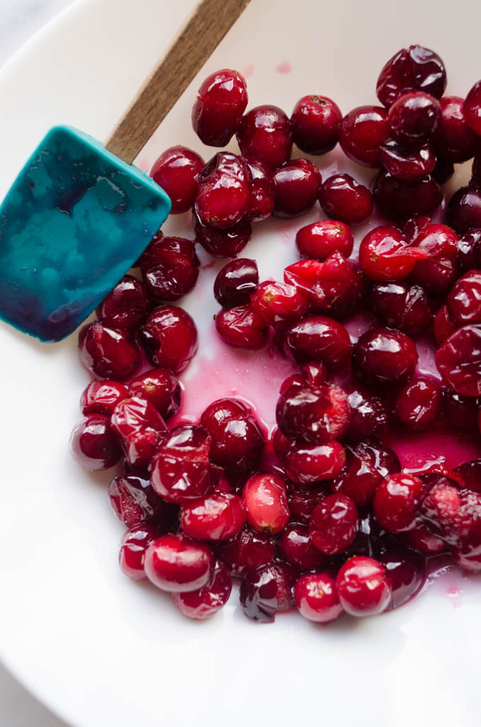 Cranberries cooked with a bit of water and maple syrup on a plate with a spatula off to the side.