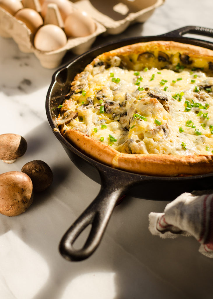 A pan of savory Dutch baby with eggs in the background and a tea towel in the foreground.