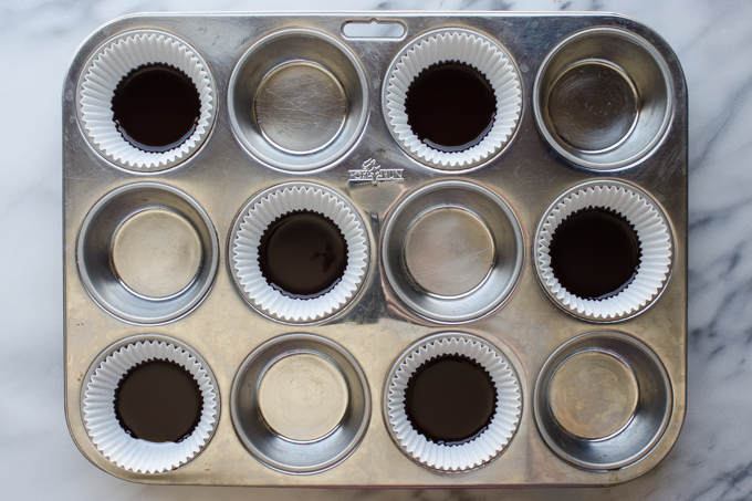 A muffin tin lined with cupcake wrappers with the chocolate base in the bottom.