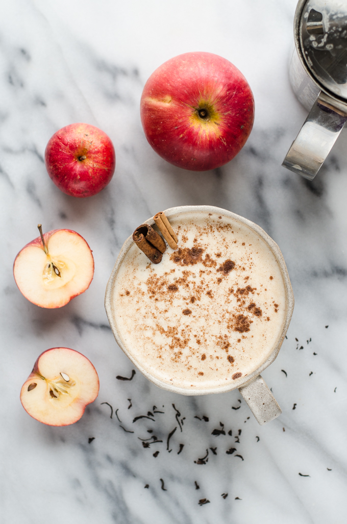 A mug of spiced Apple Tea Latte on a marble surface with apples around it.