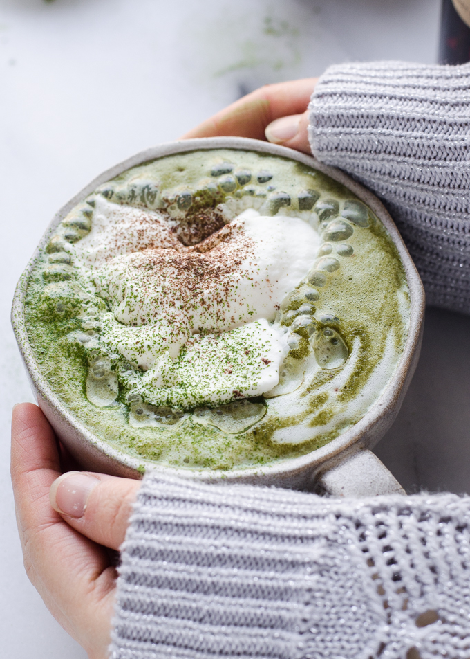 Hands around a mug of matcha cocoa, AKA matcha hot chocolate.