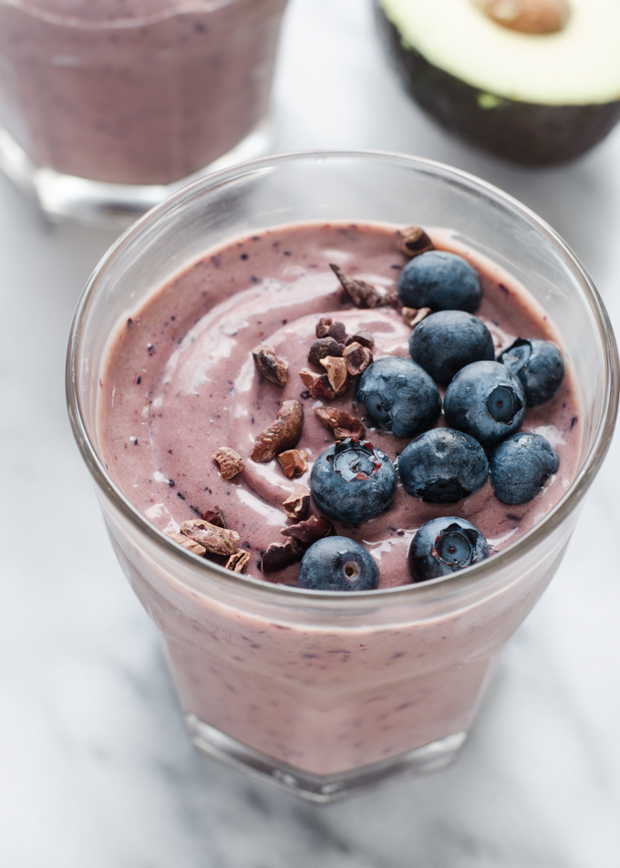 A chocolate avocado blueberry kefir smoothie on a marble surface with fresh blueberries and cacao nibs on top.