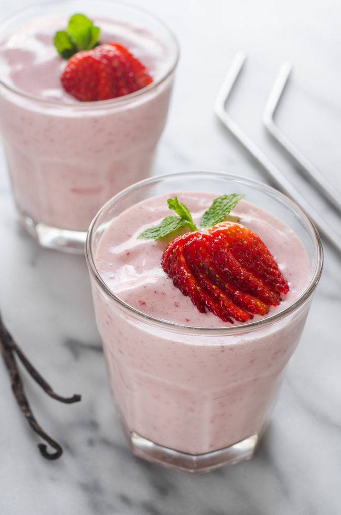 Two glasses of strawberry kefir smoothie on a marble surface with fresh strawberries on top.