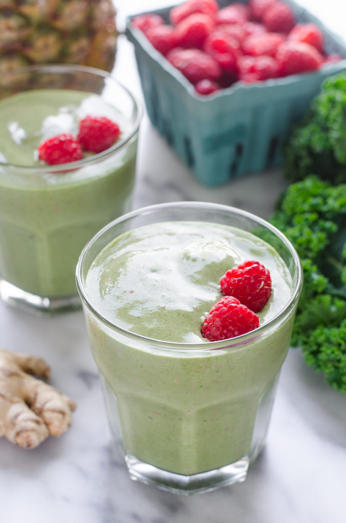 2 glasses of green smoothie made with milk kefir on a marble surface with fresh ingredients around them.