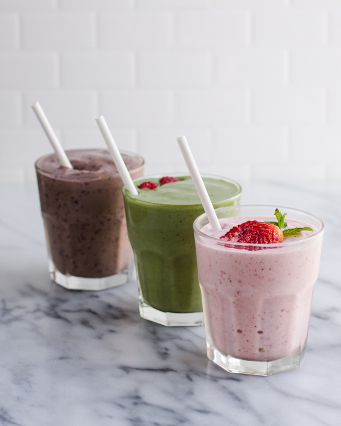 3 different healthy kefir smoothies on a marble surface with a white tile backsplash in the background.