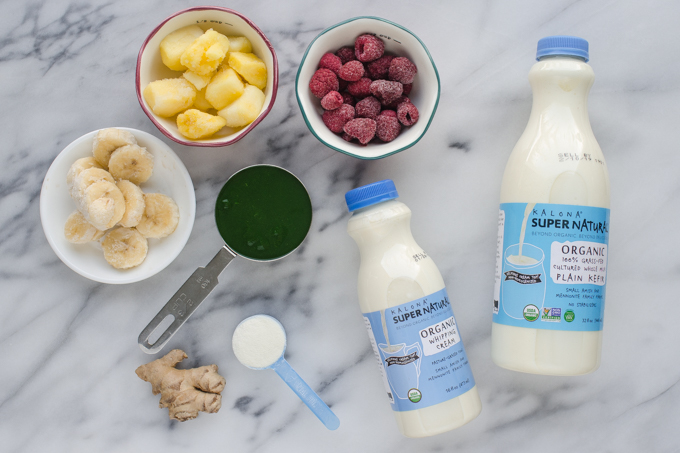 All of the ingredients needed to make a green kefir smoothie laid out on a marble surface.