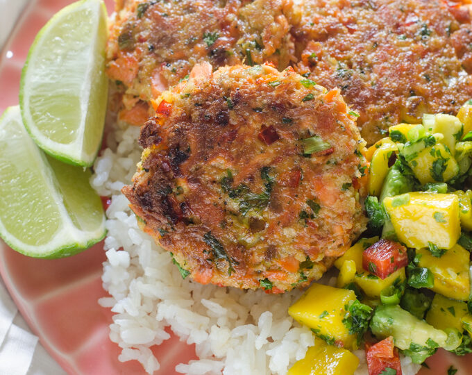 A pink plate with rice, salmon cakes, and mango salsa with lime wedges.