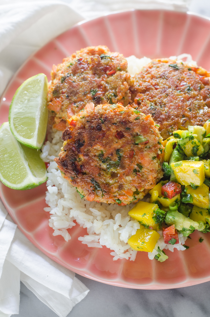 A pink plate with rice, salmon cakes, and mango salsa with lime wedges.