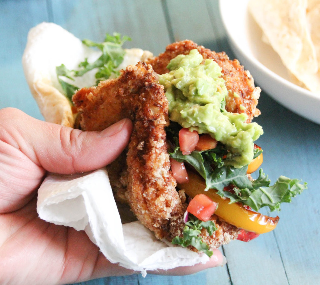 Hand holding a fried chicken taco shell with all the fixings.