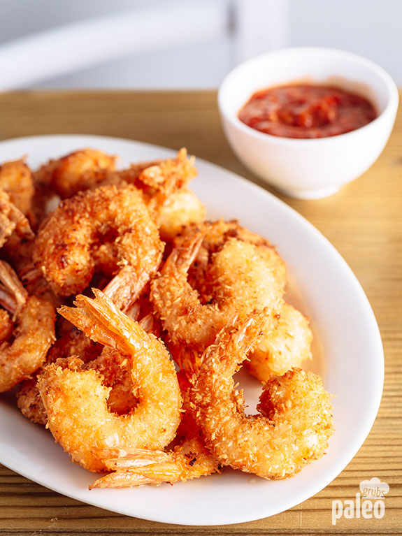 Platter of fried coconut shrimp with dipping sauce in the background.