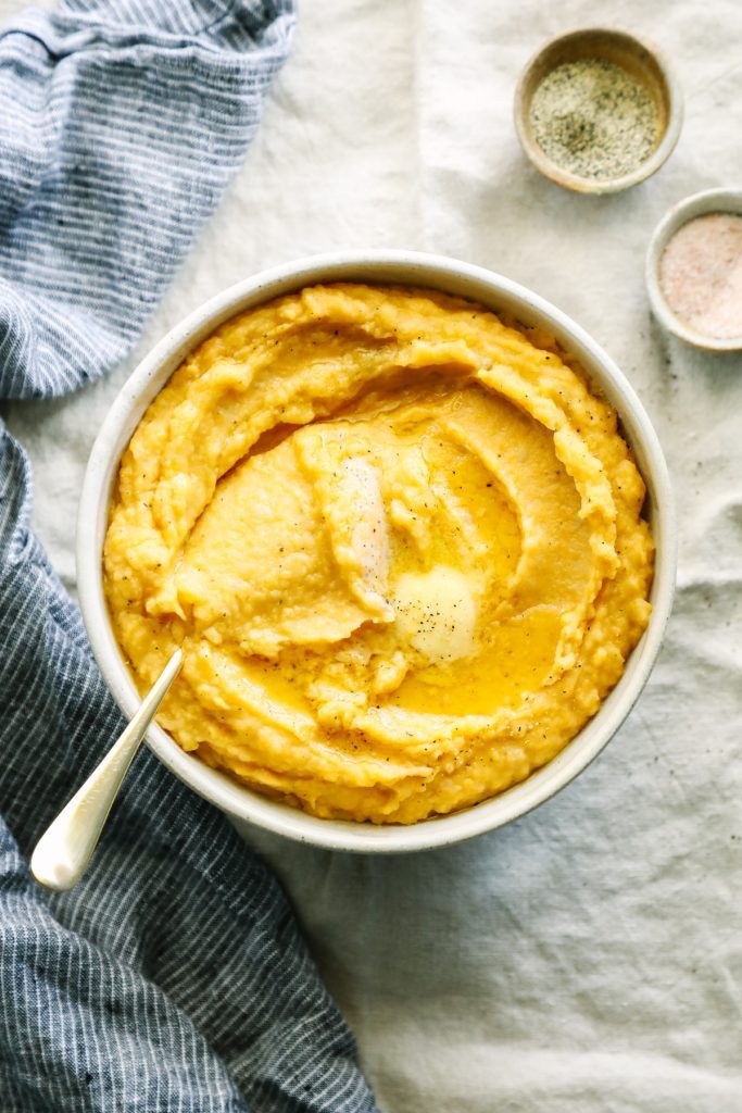 From above view of mashed squash in a serving bowl with a spoon.