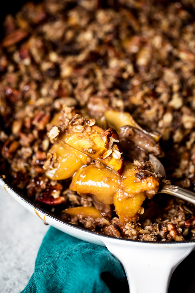 Scooping peach cobbler out of a skillet.