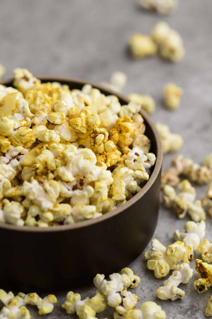 Bowl of coconut curry popcorn with pieces scattered around.