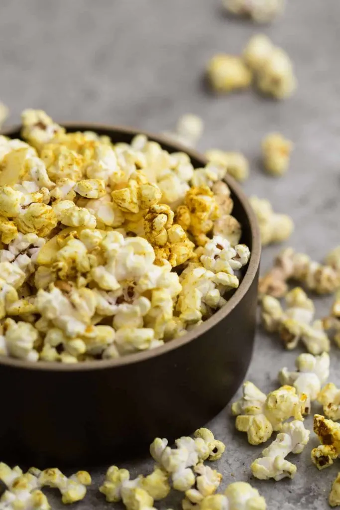 Bowl of coconut curry popcorn with pieces scattered around.