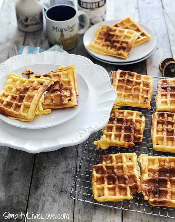 Eggnog waffles on a cooling rack and on plates with mugs in the background.