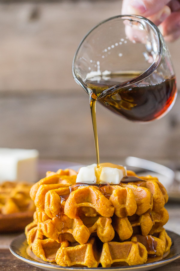 Stack of pumpkin waffles with syrup being poured on top.