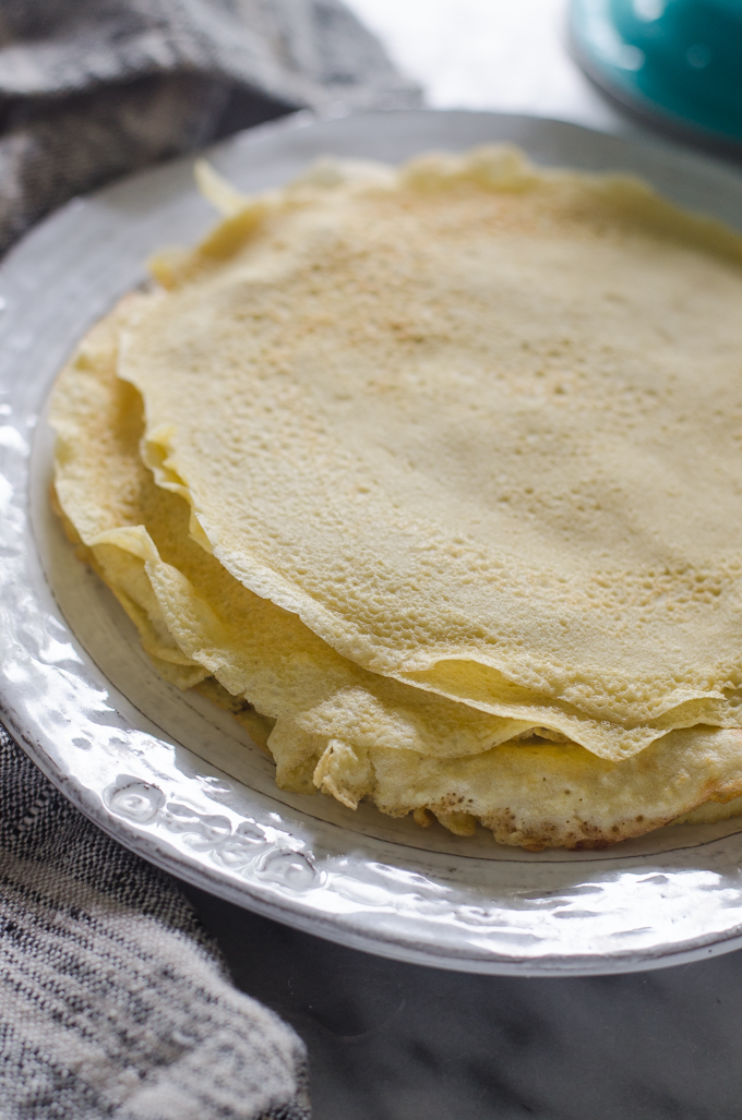 Stack of crepes on a plate with a linen napkin next to it.