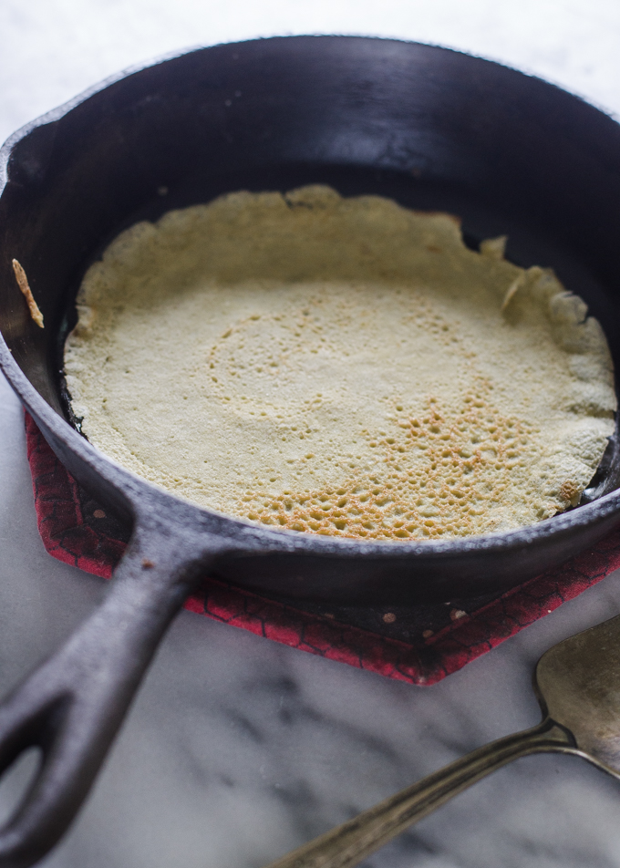 A crepe in a frying pan on a marble surface.