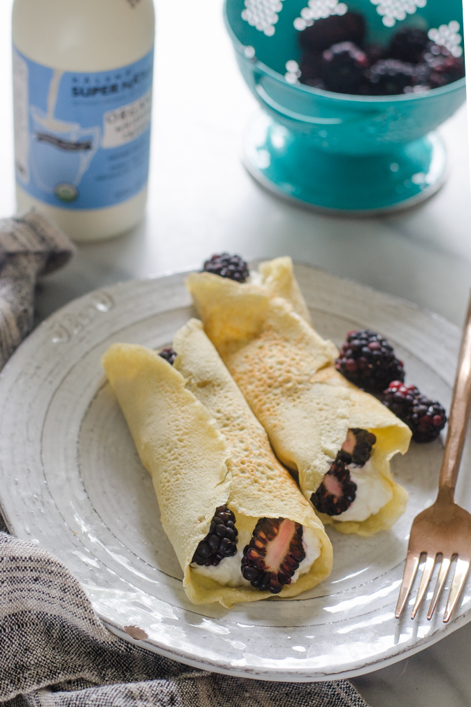 KETO crepes filled with whipped cream and blackberries on a plate on a marble surface.